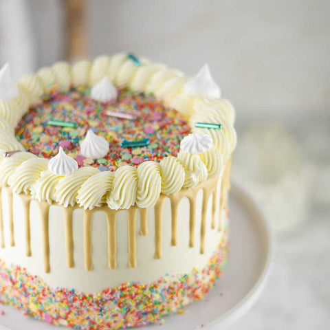 Witte taart met gouden drip en heel veel gekleurde sprinkles.