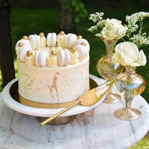 Prachtige witte taart met gouden elementen en smakelijke macarons als decoratie.